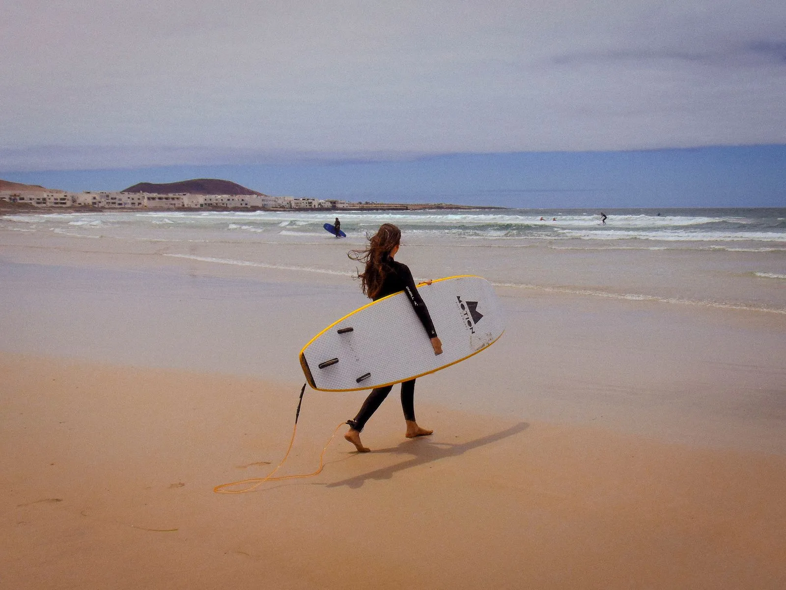 A lone surfer carrying a board along Caleta de Famara beach in Spain, perfect for summer recreation.